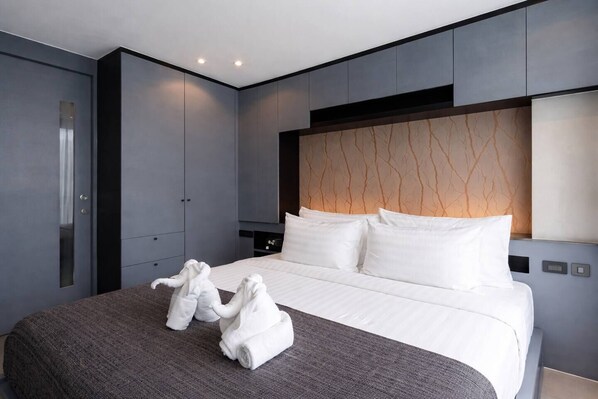Una habitación de hotel moderna con una cama grande, paredes grises y un cabecero con un diseño original.