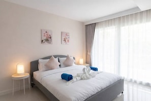 A hotel room with a bed, two bedside tables, a window with curtains, and two wall-mounted floral paintings.