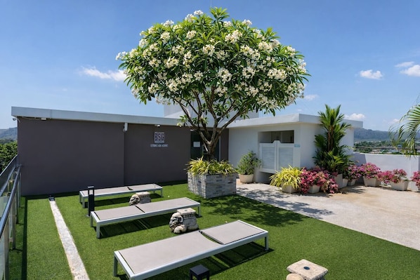 A rooftop terrace with artificial grass, seating areas, and a variety of potted plants.