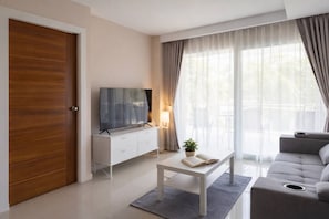 A modern living room with a flat-screen TV on a white cabinet, a grey sofa, and a coffee table with a book and a plant.