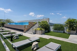A rooftop terrace with artificial grass, outdoor seating, a staircase, and a view of the landscape.