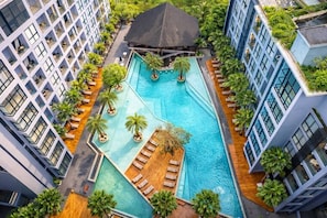 Une piscine sur le toit, entourée de bâtiments modernes dotés de balcons, de palmiers et d’espaces de détente.