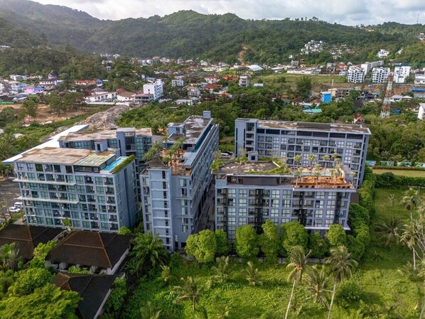 A modern multi-story building with a flat roof, surrounded by lush greenery and other residential structures.