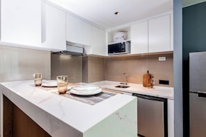 A modern kitchen with white cabinetry, stainless steel appliances, and a marble countertop.
