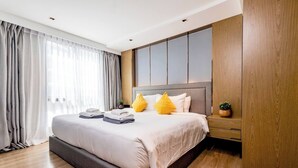 Une chambre d’hôtel moderne dotée d’un grand lit, d’un parquet, d’une armoire intégrée et d’une grande fenêtre avec des rideaux.