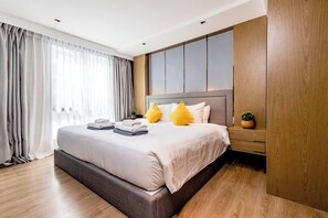 A modern hotel room with a large bed, wooden flooring, a built-in wardrobe, and a large window with curtains.