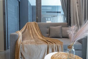 Una sala de estar moderna con un sofá gris, una silla tapizada y un jarrón con plumas de pampa.