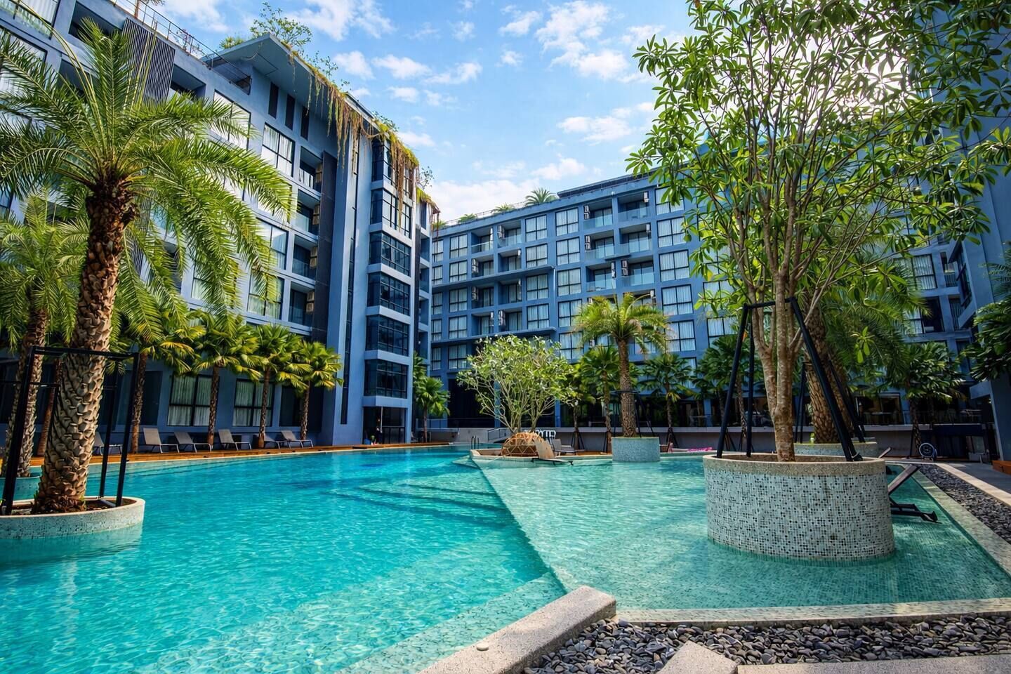 Um hotel com piscina, rodeado por palmeiras e um edifício alto com varandas.