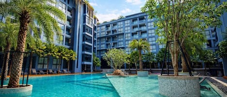 A hotel with a swimming pool surrounded by palm trees and a multi-story building with balconies.