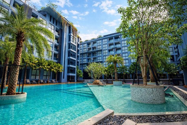 Un hotel con piscina rodeado de palmeras y un edificio de varios pisos con balcones.