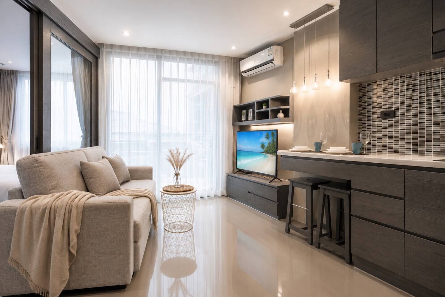A modern living room with a sofa, a TV, and a kitchen area with a tiled backsplash.