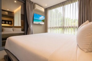 A hotel room with a bed, a television, and a window with curtains. - Vista 1br | discounted stay | Citygate Kamala (Tambon Kammala)