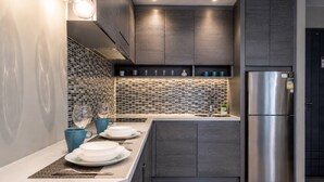 Une cuisine moderne avec un réfrigérateur en acier inoxydable, des meubles de couleur bois foncé et un pare-feu en carreaux.