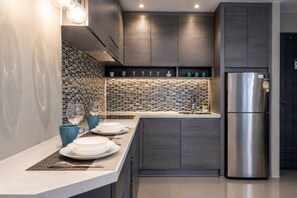 Une cuisine moderne avec un réfrigérateur en acier inoxydable, des meubles de couleur bois foncé et un pare-feu en carreaux.
