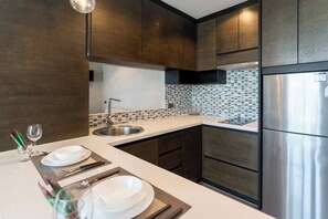 Une cuisine moderne avec des meubles de couleur sombre, un réfrigérateur en acier inoxydable et un dosseret carrelé.