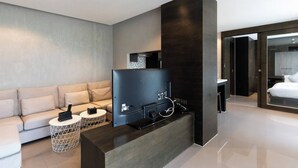 A modern hotel room with a flat-screen TV, a sofa, a coffee table, and a large window.