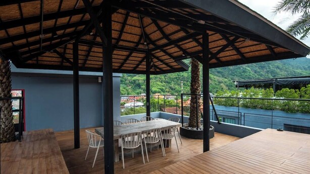An outdoor patio with a wooden deck, a covered seating area, and a view of a lush green landscape.