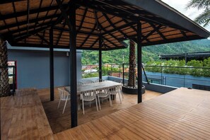 An outdoor patio with a wooden deck, a covered seating area, and a view of a lush green landscape.