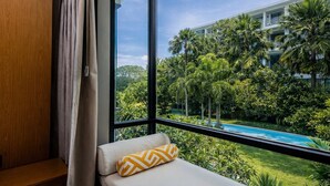 Quarto com uma grande janela com vista para uma piscina e vegetação exuberante, um banco acolchoado e um aparador de madeira.
