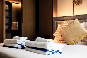 A neatly made bed with folded towels and pillows, a wooden wardrobe, and a wall-mounted decorative item.