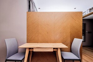 A modern room with a wooden partition, a wooden table, two grey chairs, and a dark floor.