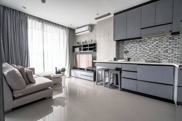 A modern kitchen with a central island, grey cabinetry, and a dining area with a sofa and curtains.