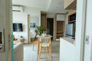 A modern kitchen with a refrigerator, microwave, and a dining area with a table and chairs. - Suite Horizon 2br|rooftop|laguna Skypark Bang tao (Choeng Thale)