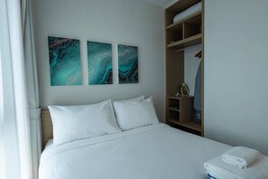 A hotel room with a bed, white bedding, a wooden wardrobe, and abstract wall art. - Suite Horizon 2br|rooftop|laguna Skypark Bang tao (Choeng Thale)