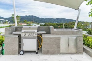 An outdoor kitchen with a grill, storage cabinet, and a hose. - Suite Horizon 2br|rooftop|laguna Skypark Bang tao (Choeng Thale)
