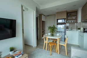 A modern kitchen with a dining area, a flat-screen TV mounted on the wall, and a small table with chairs. - Suite Horizon 2br|rooftop|laguna Skypark Bang tao (Choeng Thale)