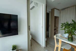 A modern living room with a flat-screen TV, a dining area with a table and chairs, and a hallway leading to a bathroom. - Suite Horizon 2br|rooftop|laguna Skypark Bang tao (Choeng Thale)