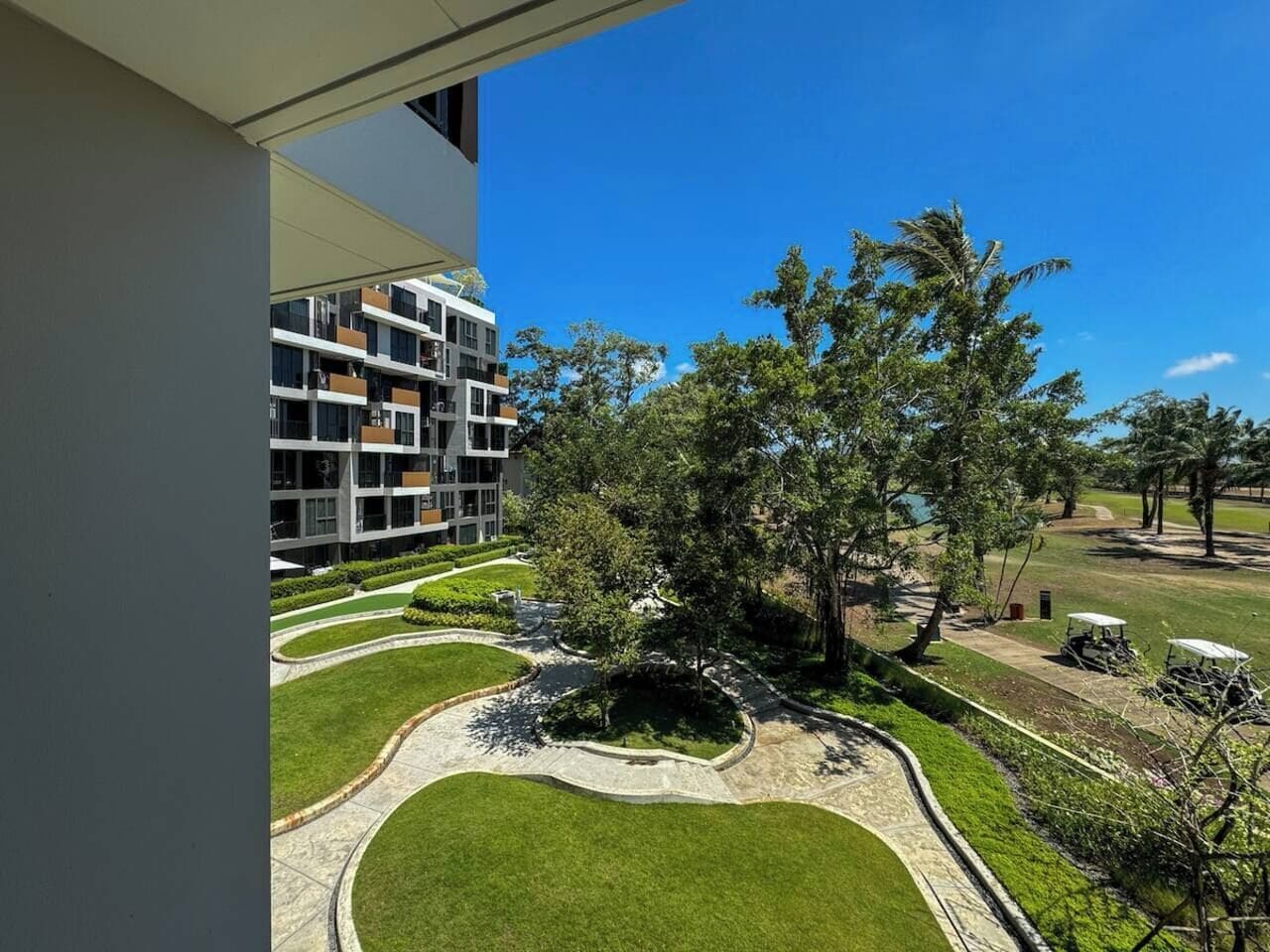 A modern building with multiple balconies, a well-maintained lawn, and a clear sky.