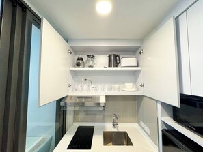 A compact kitchen with a built-in microwave, a coffee maker, and a sink. - Suite Sky 1br | Rooftop pool & gym|laguna skypark (Thep Krasatti)