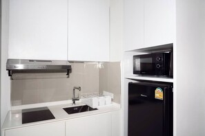 A modern kitchen with a stainless steel range hood, a microwave, and a black refrigerator. - Suite Sky 1br | Rooftop pool & gym|laguna skypark (Thep Krasatti)