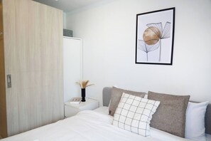 A bedroom with a bed, bedside table, and a framed artwork on the wall. - Suite Sky 1br | Rooftop pool & gym|laguna skypark (Thep Krasatti)