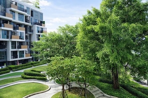 A modern multi-story building with balconies, surrounded by well-maintained greenery and a landscaped pathway.
