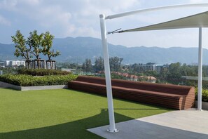 A rooftop terrace with artificial grass, a wooden bench, and a white pergola. - Suite Sky 1br | Rooftop pool & gym|laguna skypark (Thep Krasatti)