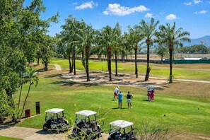 A golf course with multiple golf carts, palm trees, and a clear sky. - Suite Sky 1br | Rooftop pool & gym|laguna skypark (Thep Krasatti)