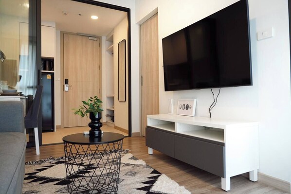 A modern living room with a flat-screen TV, a white entertainment unit, a round coffee table with a plant, and a patterned rug.