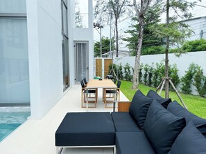 Un patio al aire libre con una mesa de comedor y sillas, un sofá negro y una piscina.