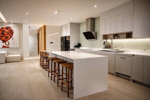 A modern kitchen with a central island, bar stools, and a large painting on the wall.