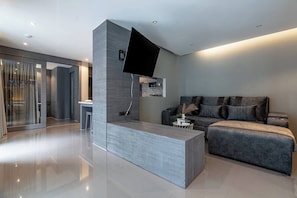 A modern living area with a grey sofa, a flat-screen TV mounted on a wall, and a small side table with a book and a plant.