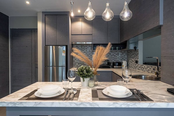 A modern kitchen with a built-in refrigerator, a dining area with a marble countertop, and pendant lighting.