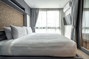 Een moderne hotelkamer met een groot bed, grijze gordijnen, een behang met patroon en een wandtelevisie.