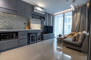 A modern living room with a sofa, a TV, and a kitchen area with a microwave.