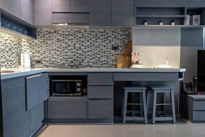 A modern kitchen with a built-in microwave, a coffee machine, and a small dining area with stools.