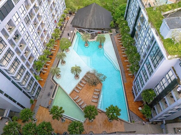 A multi-story hotel with a rooftop pool area, including lounge chairs and a small garden.