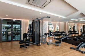 Une salle de sport moderne équipée de divers appareils d’exercice, dotée d’un grand miroir et d’un plancher en bois.