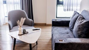 Un saló modern amb un sofà gris, una taula de centre blanca amb un ram i un comandament a distància, i un terra de fusta.