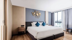 Et moderne hotelværelse med en stor seng, et natbord, en dekorativt ophængt genstand på væggen og udsigt til det fri gennem vinduet.